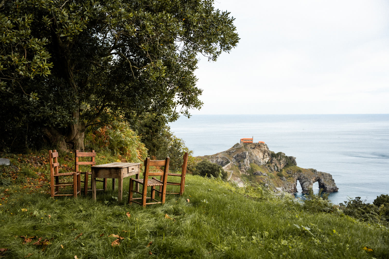 Mesa y sillas tradicionales bajo la encina frente a San Juan de Gaztelugatxe
