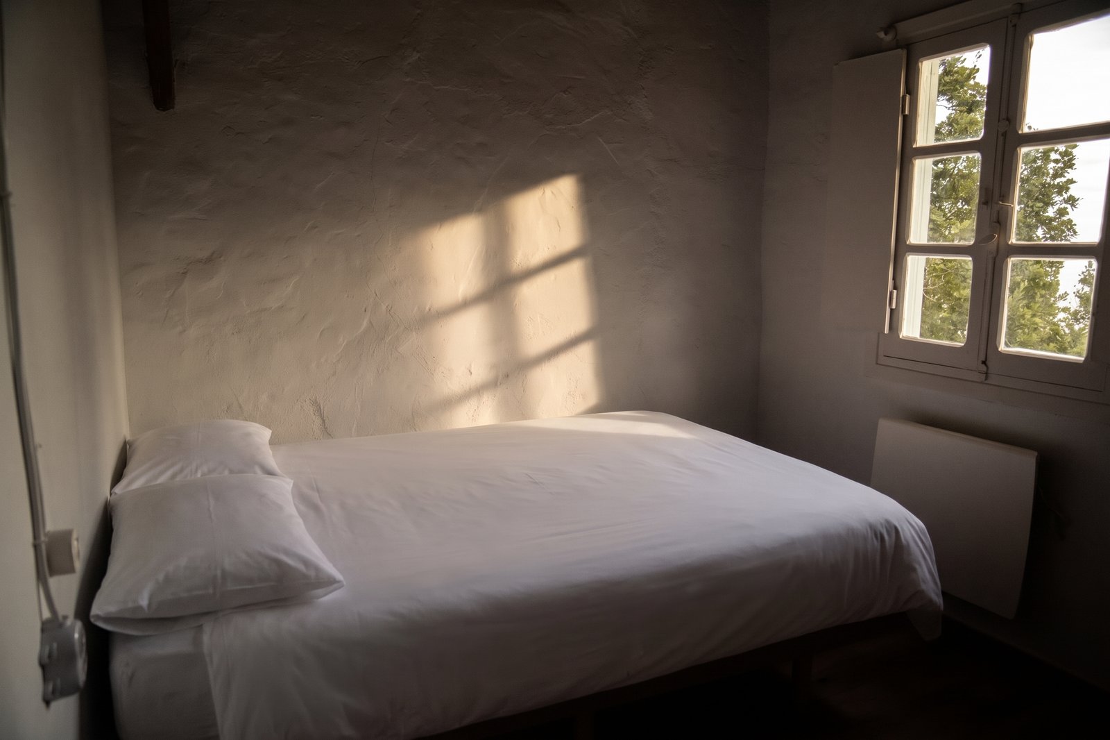 Sombras cálidas sobre muros a la cal en habitación doble